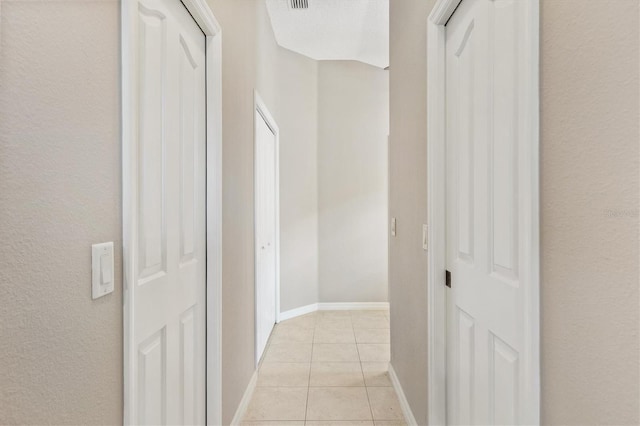 hall with light tile patterned flooring, visible vents, and baseboards