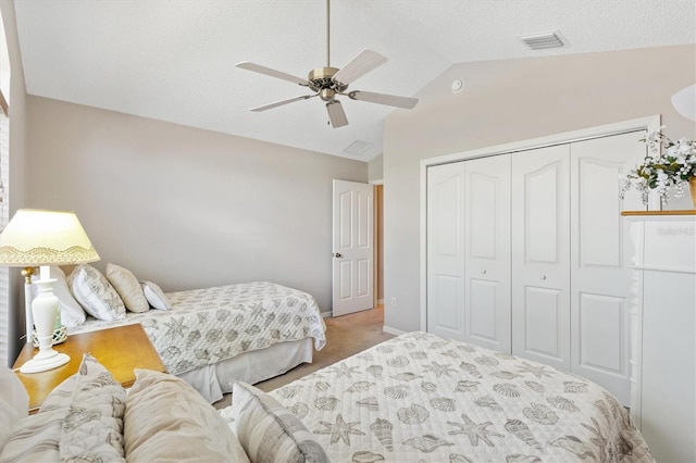 carpeted bedroom with a ceiling fan, visible vents, lofted ceiling, a closet, and a textured ceiling