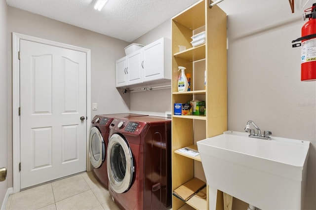 washroom with washer and clothes dryer, a sink, a textured ceiling, cabinet space, and light tile patterned floors