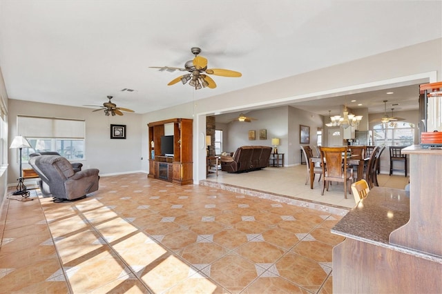 living area featuring light tile patterned floors, visible vents, baseboards, and ceiling fan