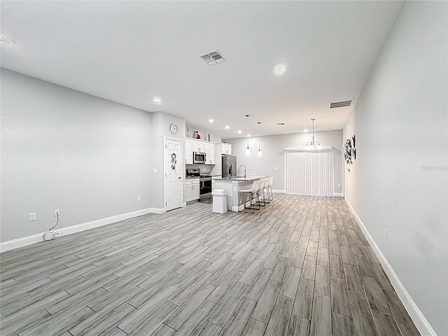 unfurnished living room featuring a sink, visible vents, baseboards, and light wood-style floors