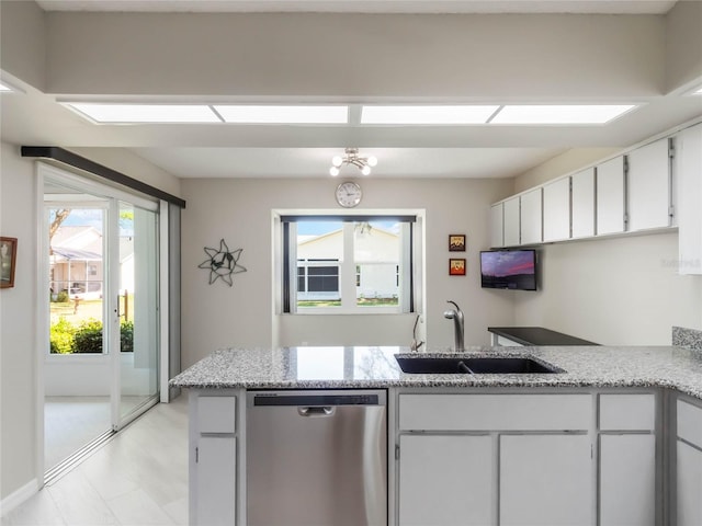 kitchen featuring a sink, stainless steel dishwasher, a peninsula, white cabinets, and light stone countertops