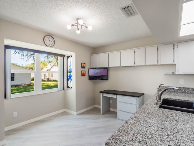 kitchen featuring white cabinetry, visible vents, built in desk, and a sink