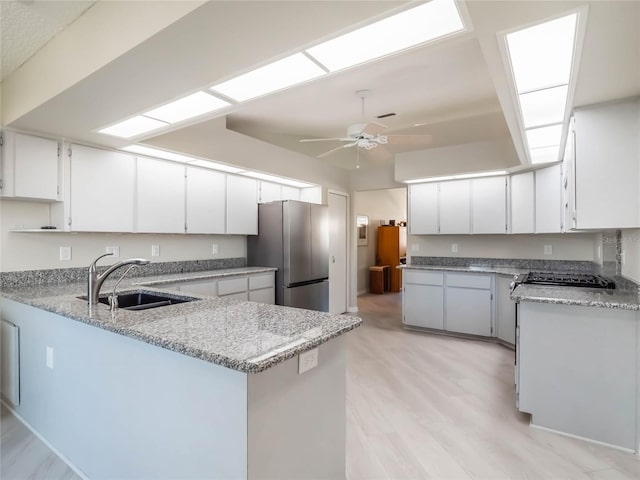 kitchen featuring a sink, freestanding refrigerator, light wood-style floors, a peninsula, and ceiling fan