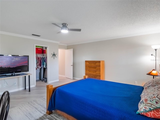 bedroom featuring a ceiling fan, visible vents, a spacious closet, a textured ceiling, and crown molding