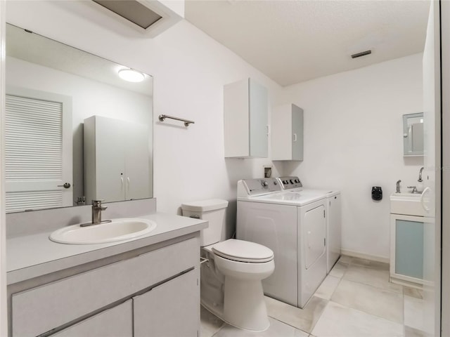 bathroom with independent washer and dryer, toilet, two vanities, and a sink