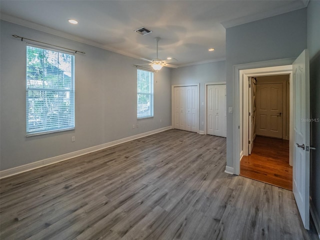 unfurnished bedroom with two closets, crown molding, baseboards, recessed lighting, and wood finished floors