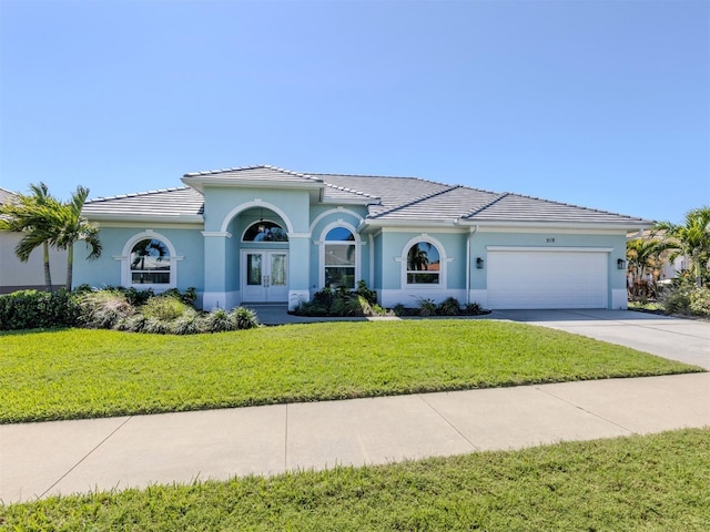 mediterranean / spanish-style home featuring concrete driveway, a front yard, stucco siding, french doors, and a garage