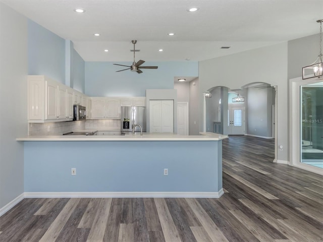 kitchen with ceiling fan with notable chandelier, stainless steel fridge, arched walkways, a peninsula, and light countertops