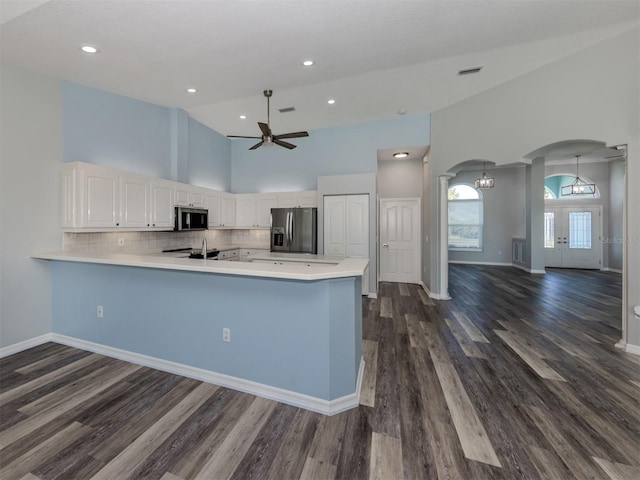 kitchen featuring tasteful backsplash, stainless steel appliances, arched walkways, a peninsula, and light countertops