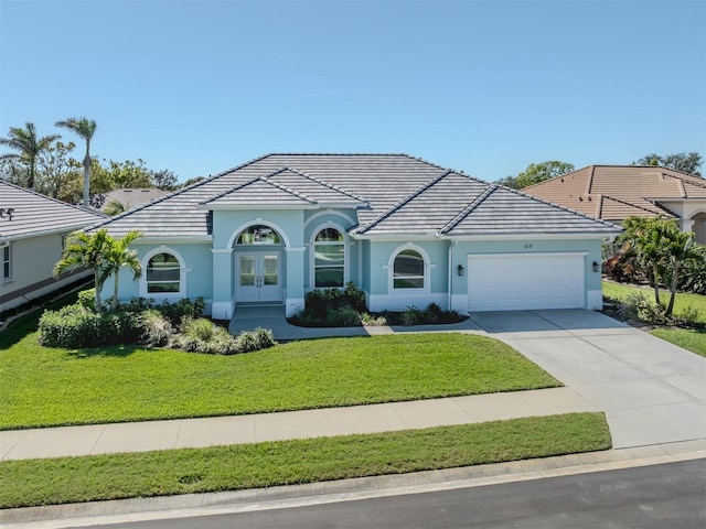 view of front of property with a front lawn, a tile roof, concrete driveway, french doors, and an attached garage