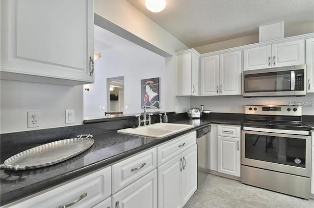 kitchen with white cabinetry, dark countertops, appliances with stainless steel finishes, and a sink