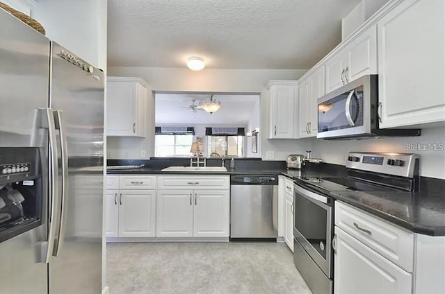 kitchen with dark countertops, appliances with stainless steel finishes, white cabinets, a textured ceiling, and a sink