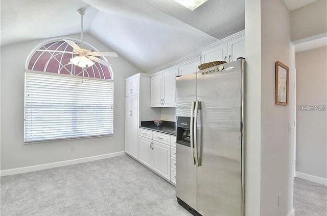 kitchen featuring dark countertops, lofted ceiling, light carpet, stainless steel refrigerator with ice dispenser, and white cabinets