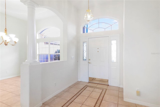 tiled entrance foyer featuring a notable chandelier, a high ceiling, baseboards, and decorative columns