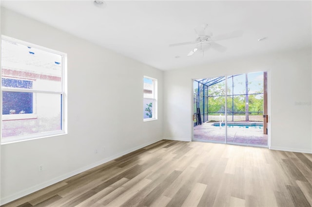 unfurnished room featuring baseboards, wood finished floors, a ceiling fan, and a sunroom