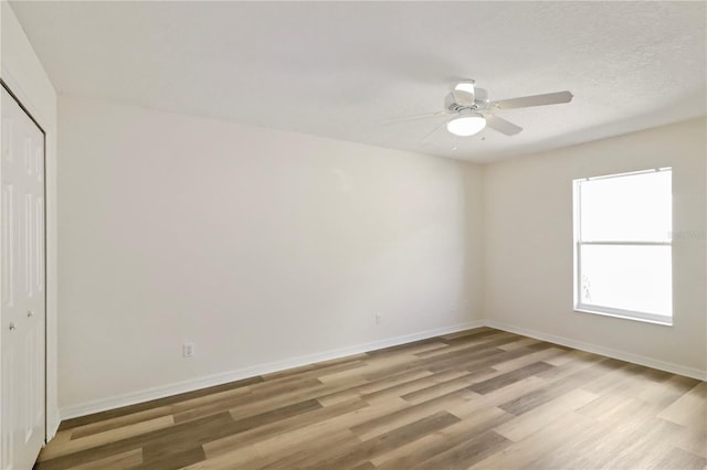 spare room featuring light wood-style flooring, a ceiling fan, and baseboards