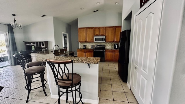 kitchen featuring a sink, decorative backsplash, black appliances, a kitchen breakfast bar, and brown cabinets