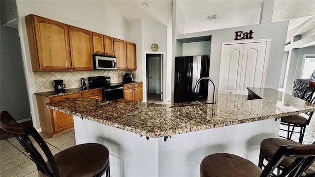 kitchen with visible vents, backsplash, brown cabinets, a kitchen breakfast bar, and black appliances