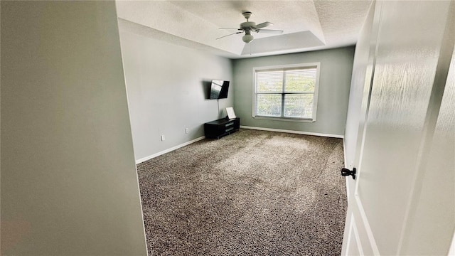 carpeted spare room featuring baseboards, a raised ceiling, a textured ceiling, and a ceiling fan