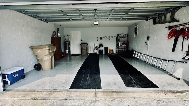 garage with concrete block wall, a garage door opener, and water heater