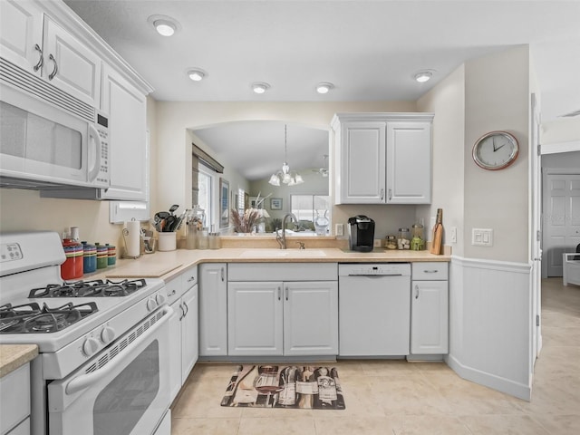 kitchen featuring a wainscoted wall, a sink, white cabinetry, white appliances, and light countertops