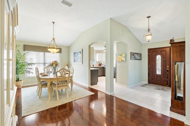 foyer entrance featuring light wood-type flooring, arched walkways, a textured ceiling, and lofted ceiling