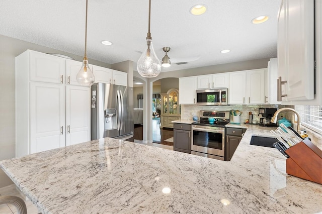 kitchen with backsplash, light stone countertops, appliances with stainless steel finishes, arched walkways, and a sink