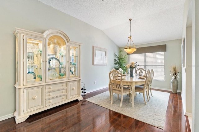 dining area with a textured ceiling, dark wood-type flooring, baseboards, and vaulted ceiling