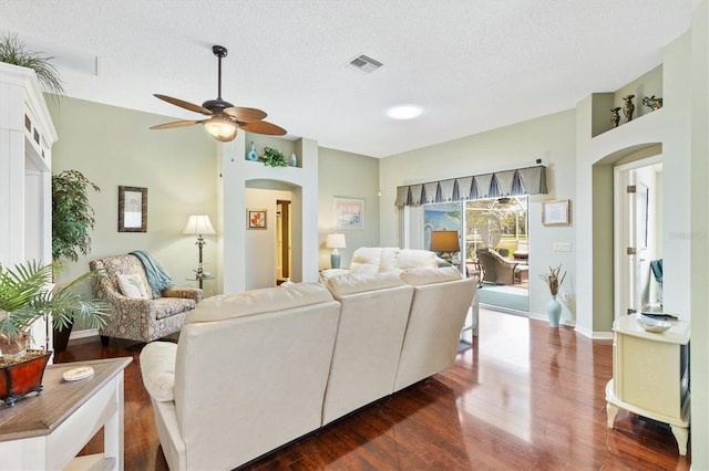 living room featuring arched walkways, visible vents, a textured ceiling, and dark wood-style floors