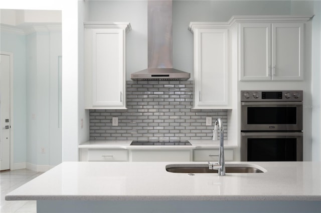 2174 Wallingford Loop, Mount Dora, FL 32757 - kitchen with wall chimney range hood, stainless steel double oven, black electric cooktop, and decorative backsplash