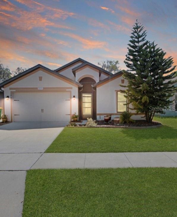 view of front of house with stucco siding, an attached garage, concrete driveway, and a front yard