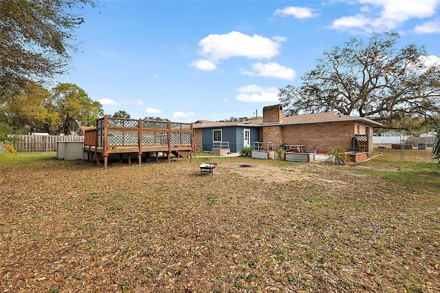 rear view of property featuring fence, a yard, a fire pit, a deck, and brick siding