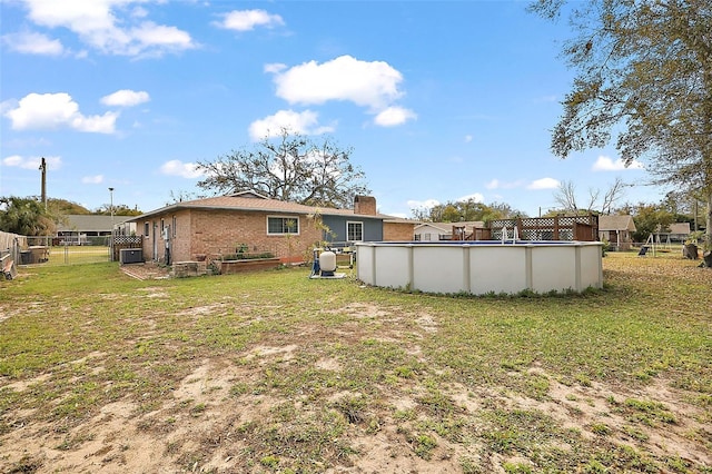 rear view of house with a gate, fence, an outdoor pool, a lawn, and brick siding