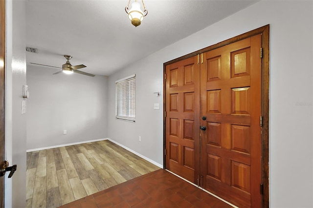 foyer with ceiling fan, visible vents, baseboards, and wood finished floors