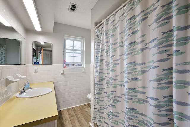 bathroom with visible vents, toilet, wainscoting, wood finished floors, and tile walls