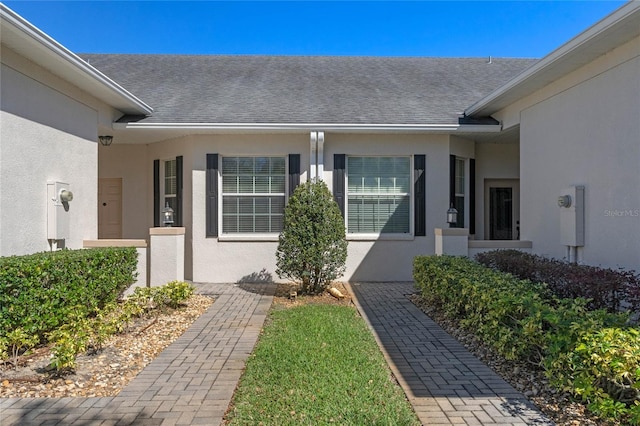 doorway to property with a shingled roof and stucco siding