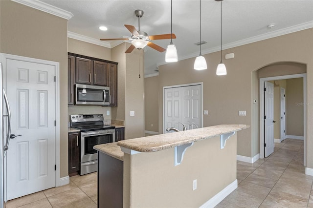 kitchen featuring a breakfast bar, an island with sink, arched walkways, stainless steel appliances, and dark brown cabinets