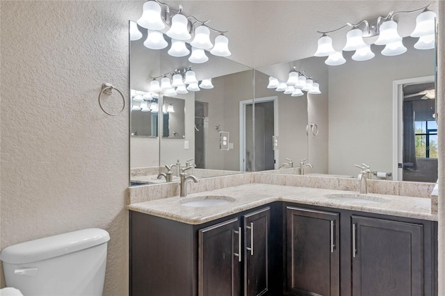 bathroom with double vanity, toilet, a textured wall, and a sink