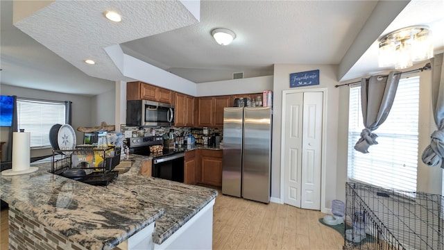 kitchen featuring visible vents, dark stone counters, brown cabinets, a peninsula, and stainless steel appliances