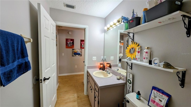 bathroom with visible vents, toilet, vanity, wood finished floors, and a textured ceiling