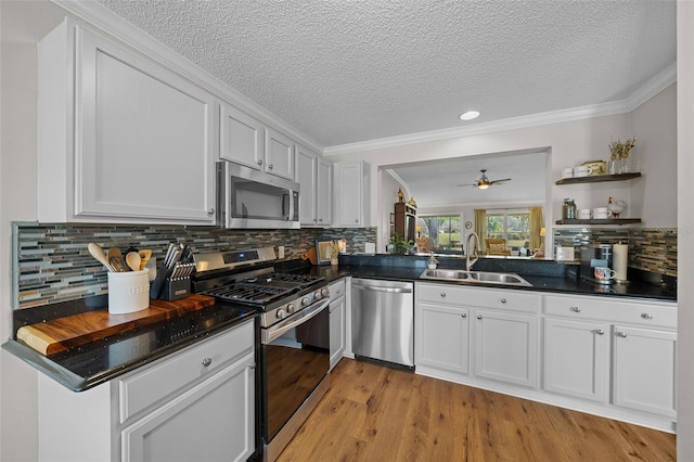 kitchen with open shelves, a sink, appliances with stainless steel finishes, dark countertops, and light wood-type flooring