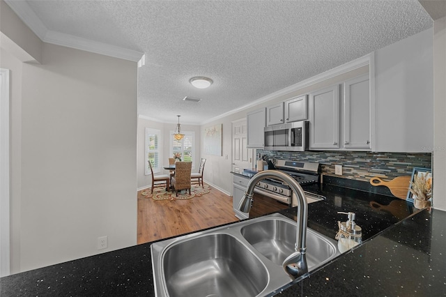 kitchen with a sink, decorative backsplash, ornamental molding, stainless steel appliances, and light wood-type flooring