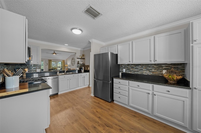 kitchen featuring dark countertops, visible vents, light wood-type flooring, ornamental molding, and appliances with stainless steel finishes