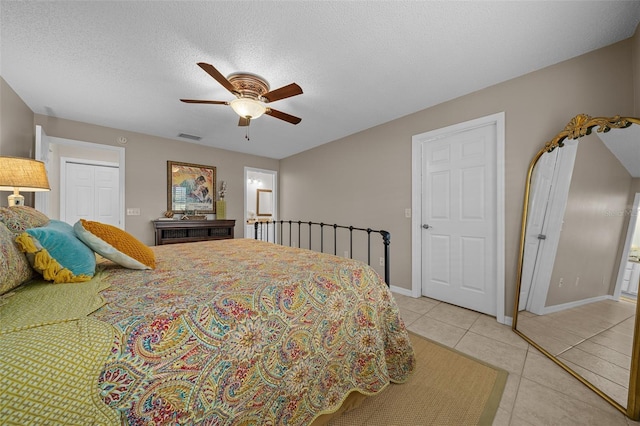 bedroom featuring visible vents, a ceiling fan, a textured ceiling, light tile patterned floors, and baseboards