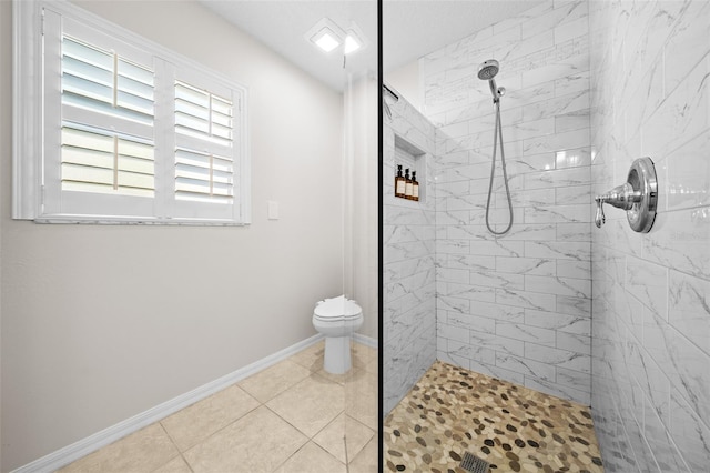 bathroom featuring a tile shower, tile patterned floors, toilet, and baseboards