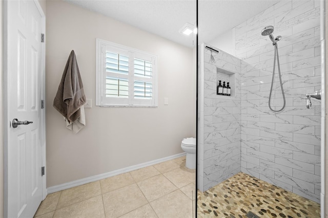 bathroom with tile patterned floors, toilet, a textured ceiling, tiled shower, and baseboards