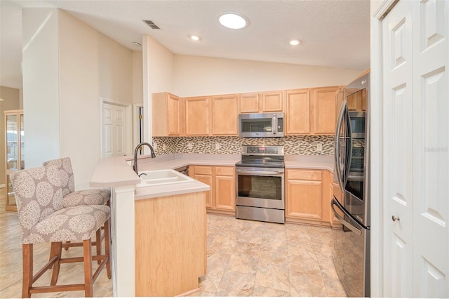 kitchen with a peninsula, light brown cabinets, appliances with stainless steel finishes, and a sink