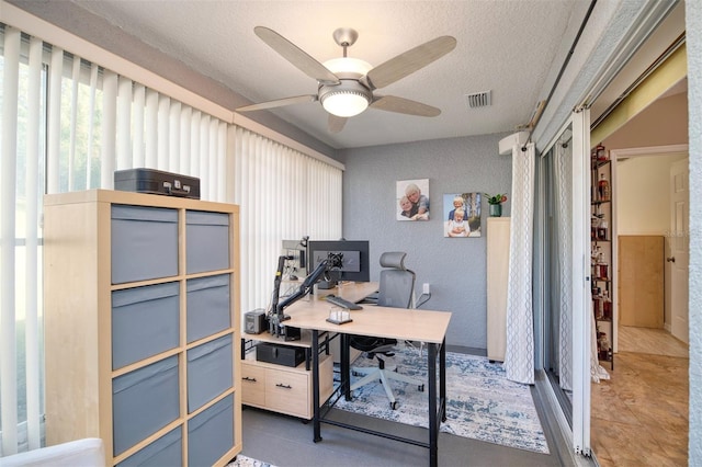 tiled office space featuring visible vents, a textured ceiling, ceiling fan, and a textured wall