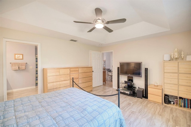 bedroom with light wood-type flooring, a tray ceiling, visible vents, and a ceiling fan